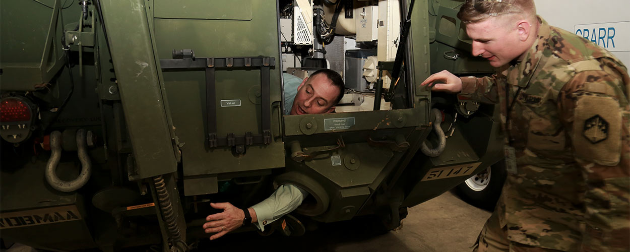 Peter Emanuel, Ph.D., reaches for the exterior sampling arm from inside an NBCRV, experiencing, first hand, the challenges Soldiers like Sgt. Ryan Ashley must manage during training and deployment.