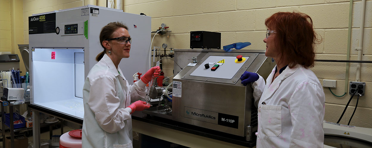 Researchers Calm and Betts confer while breaking down cell membranes using a microfluidizer.