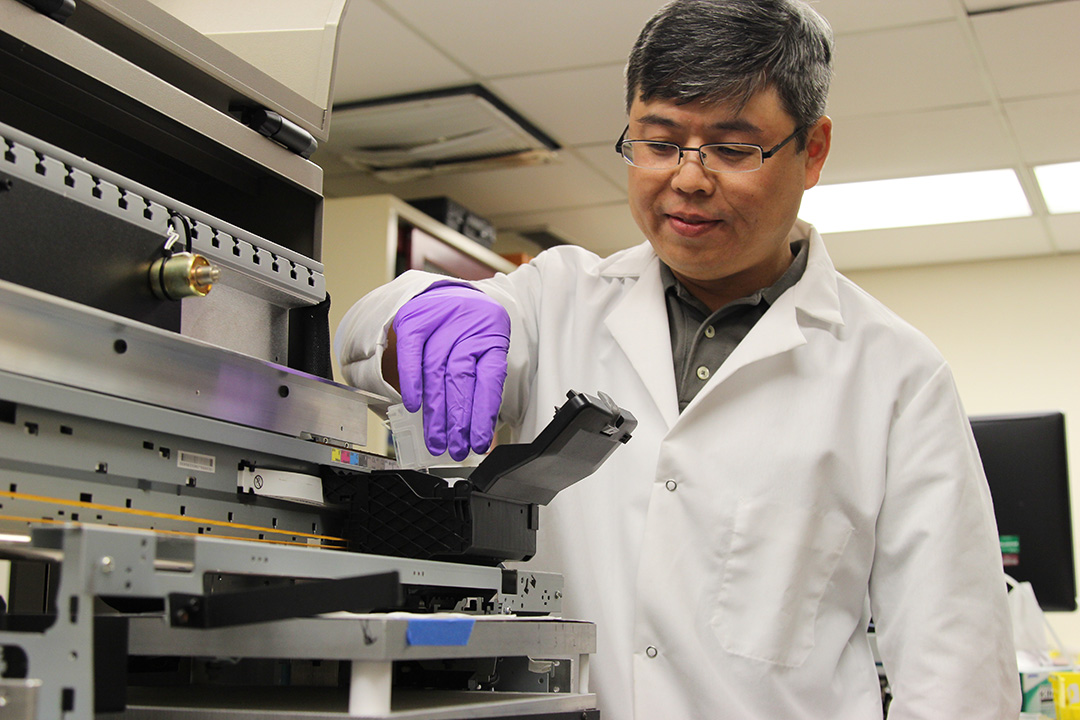 Kevin Hung, software engineer at DEVCOM CBC, loads the modified inkjet printer cartridges into the system at the spectroscopy branch’s inkjet printing laboratory for testing. (U.S. Army photo by Ellie White)